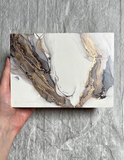 Grey and gold art featuring fantasy art of wings hand painted in an abstract, marble stone technique. This original painting for sale is held above a stone backdrop.