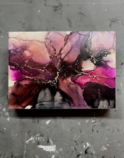 Abstract art of space featuring pink, purple, black, copper and gold colours on a textured grey background; celestial wall art.