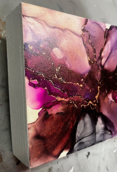 Abstract artwork of space and lightning. Pink, purple, black, copper and gold colours collide in this space art that sits on a grey background.