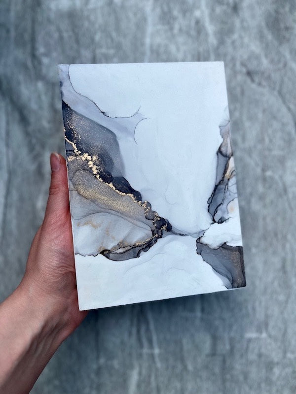 Ethereal and surreal gothic fantasy art for gallery walls featuring grey and gold fantasy wings, held in a hand above a grey stone wall. This wing art piece is symbolic of dreams.