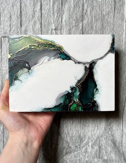 Original art for gallery walls featuring fantasy dragon wings in jewel tones of gothic green and gold. This fantasy art piece is held in a hand above a stone backdrop.