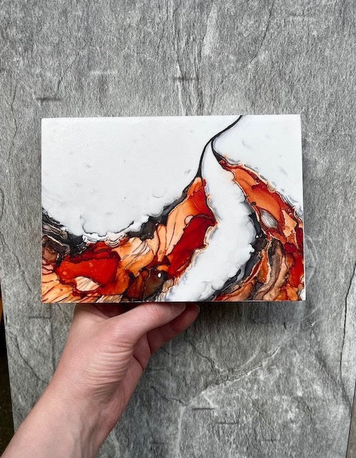 Fantasy art featuring fantasy wings in orange, red and black shades, symbolic of transformation and rebirth and inspired by the fire bird in mythology tales, the phoenix. This original painting is held above a stone backdrop.
