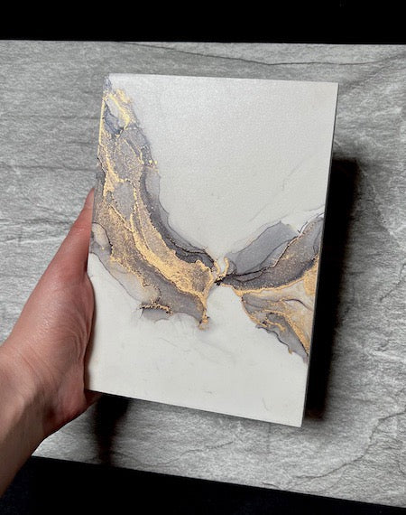 A surreal wing painting forged in grey and gold ink, SKYLINE conjures up the gloom and glow of smoke and fractured light. An otherworldly painting held above a neutral stone backdrop.