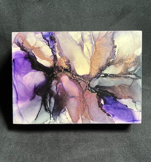 A space painting featuring the remnants of a supernova in shades of purple, black, copper and white in an abstract design. This 5x7 art is an original painting, hand painted and set on a dark backdrop.